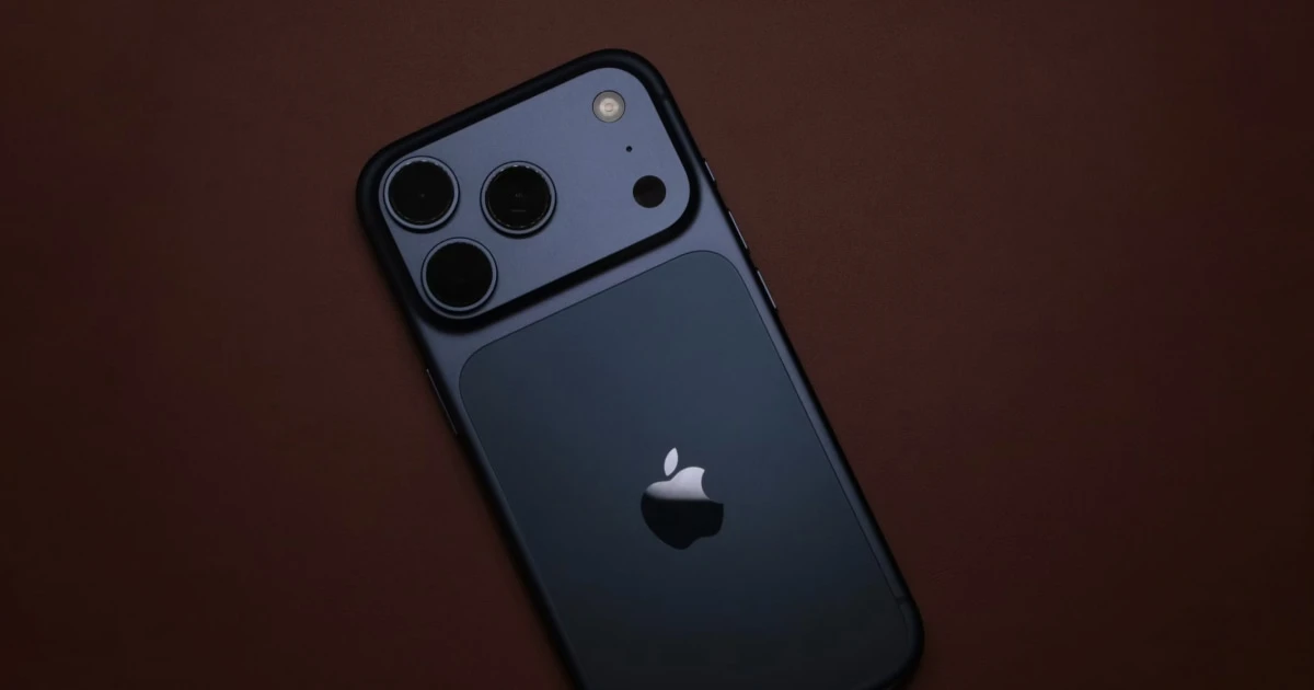 Back of a dark blue iPhone with a triple camera on a deep brown surface.