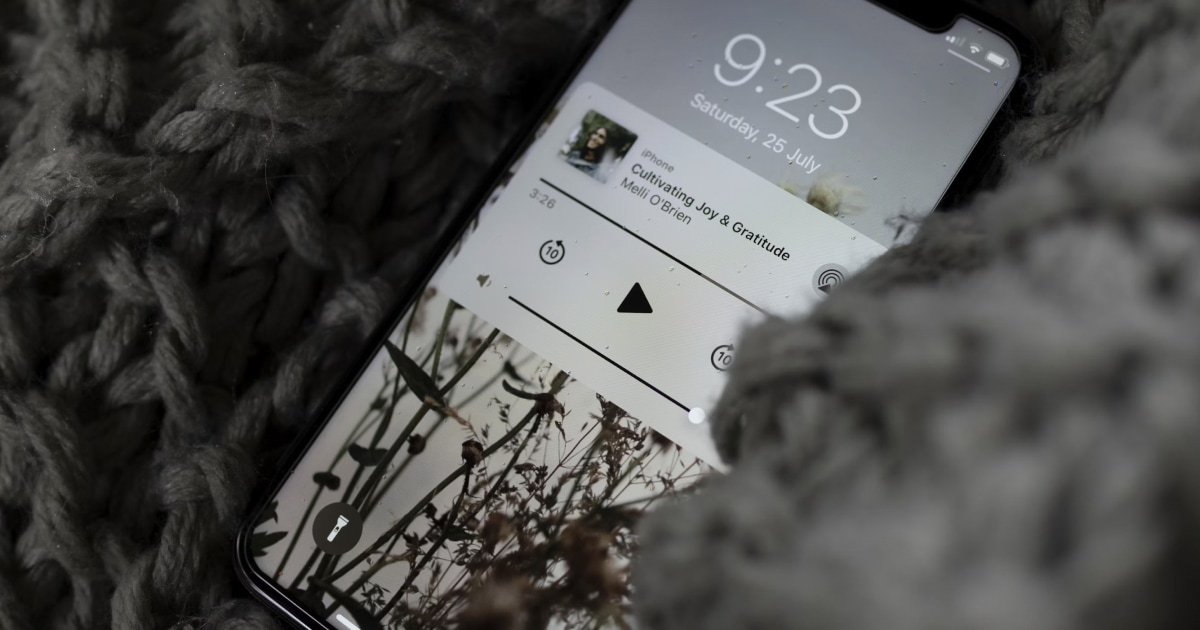 iPhone lock screen showing an audio player, resting among soft chunky knit blankets.