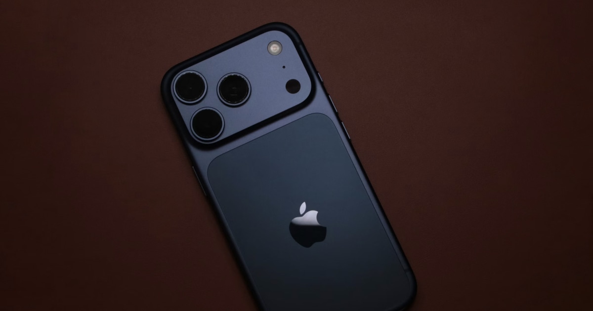 Back of a dark blue iPhone with a triple camera on a deep brown surface.