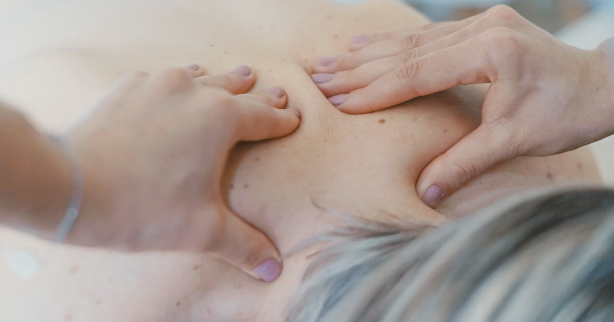 Close-up of two hands massaging a person's back.