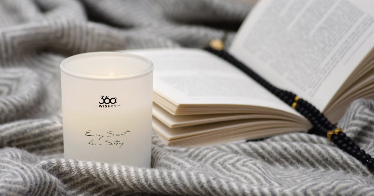 Lit white candle, an open book and prayer beads on a gray woolen blanket.